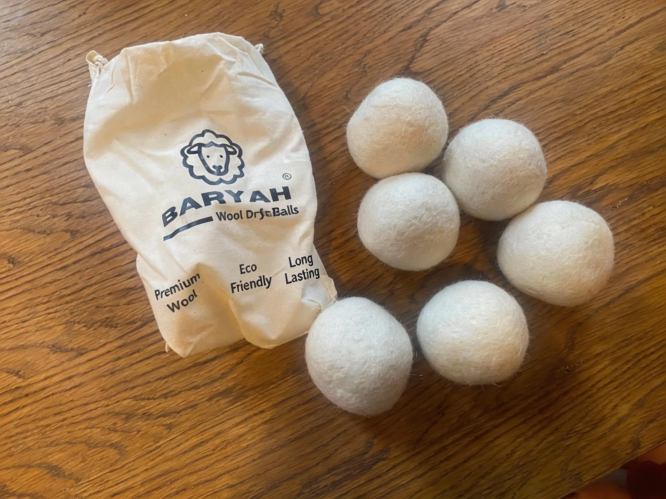 Six natural wool balls and a BARYAH cotton bag on a wooden tabletop
